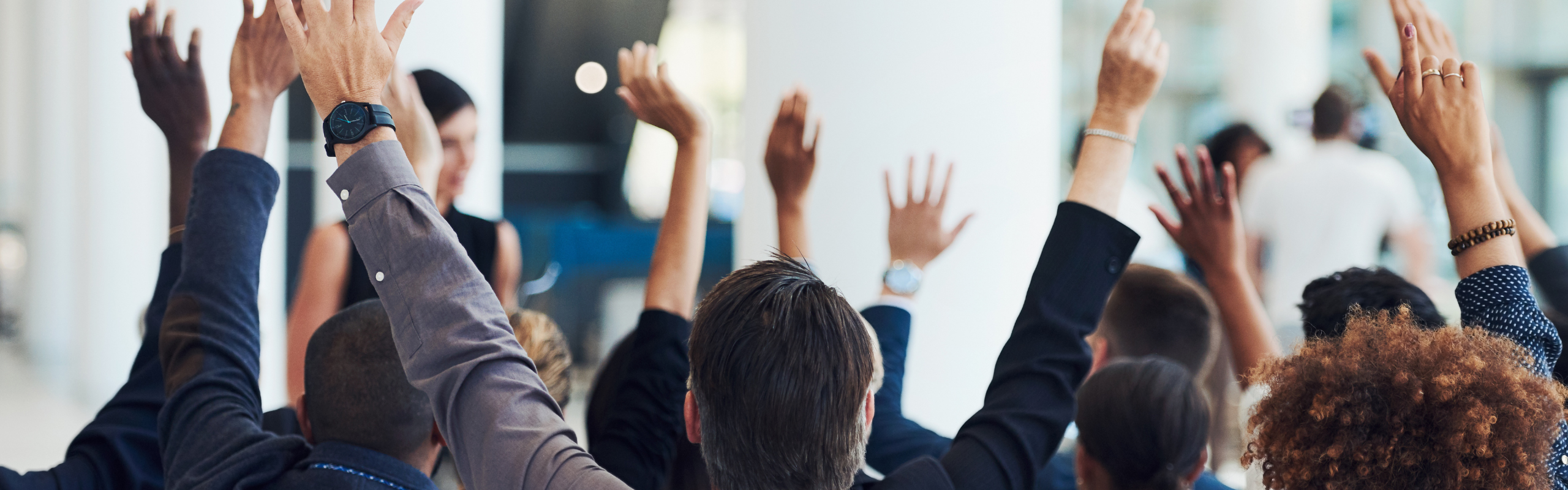 A group of business professionals raise their hands together in celebration at an indoor meeting.